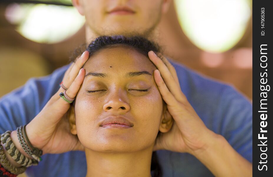 Natural lifestyle portrait of young beautiful and relaxed Asian Balinese woman receiving a healing facial and head Thai massage by