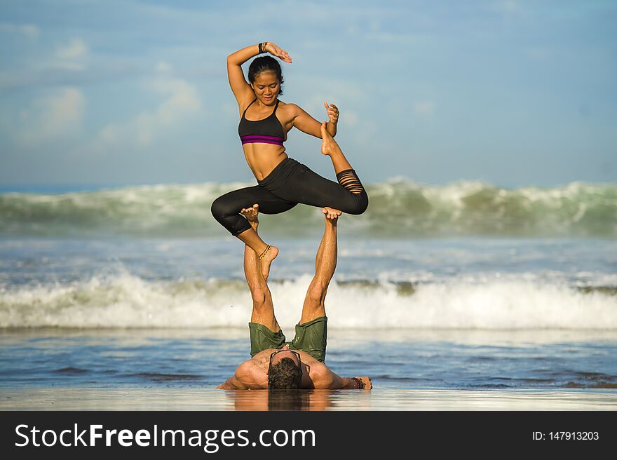Outdoors lifestyle portrait young attractive and concentrated couple of yoga acrobats practicing acroyoga balance and meditation exercise on beautiful beach in mind and body teamwork control