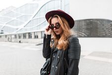 Sexy Pretty Young Hipster Woman In Sunglasses In Vintage Hat In Trendy Leather Jacket With Black Backpack Stands Stock Images