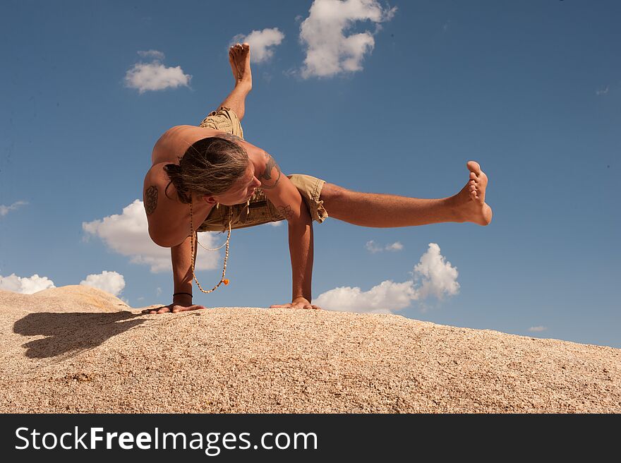 Male yogi hand balancing in Flying Splits or in Sanskrit Eka Pada Koundinyasana on a boulder field on a sunny cloud filled day. This pose is dedicated to the sage Koundinya II. Photographed in  Joshua Tree, CA a wilderness desert environment. Male yogi hand balancing in Flying Splits or in Sanskrit Eka Pada Koundinyasana on a boulder field on a sunny cloud filled day. This pose is dedicated to the sage Koundinya II. Photographed in  Joshua Tree, CA a wilderness desert environment.