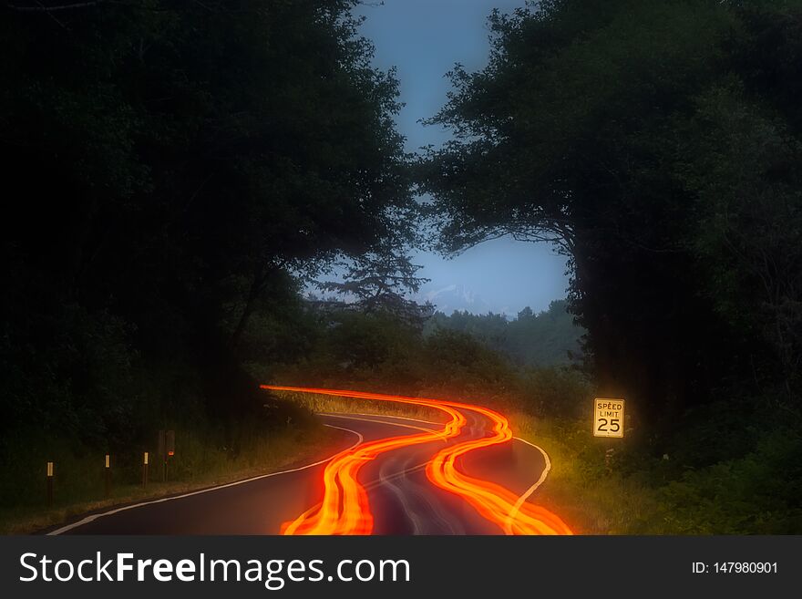 Orange, red and yellow car light trails along a road curve in the mountains at night with speed limit sign. Transportation