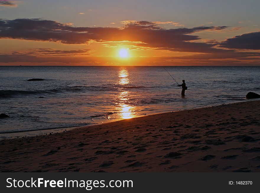 Fisherman surf-fishing at sunset on a rocky Atlantic Ocean beach. Fisherman surf-fishing at sunset on a rocky Atlantic Ocean beach.