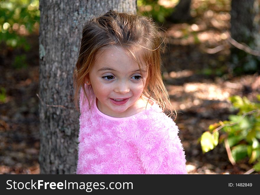 Beautiful little girl standing outdoors by a tree. She's smiling and looking as something has her attention. She's wearing a pink fuzzy shirt. Beautiful little girl standing outdoors by a tree. She's smiling and looking as something has her attention. She's wearing a pink fuzzy shirt.