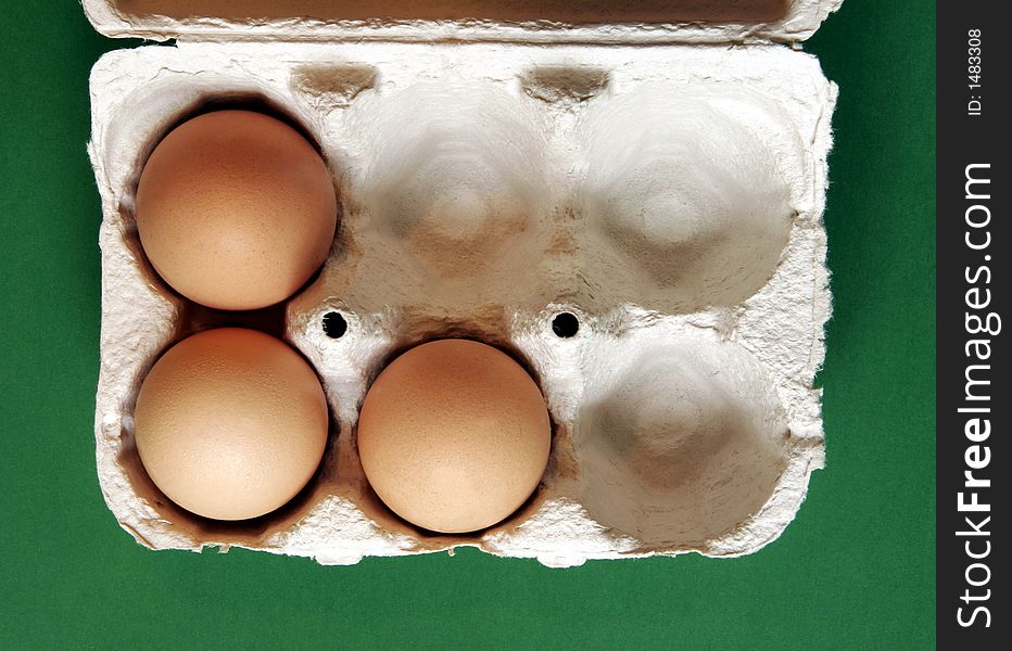 Three Brown Eggs In A Grey Cardboard Box On Green Background. Three Brown Eggs In A Grey Cardboard Box On Green Background