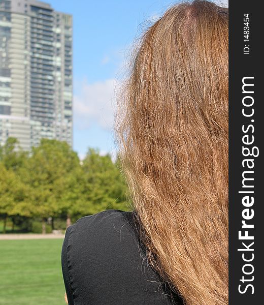 A young woman looks at a high-rise building looming over a city park. A young woman looks at a high-rise building looming over a city park.