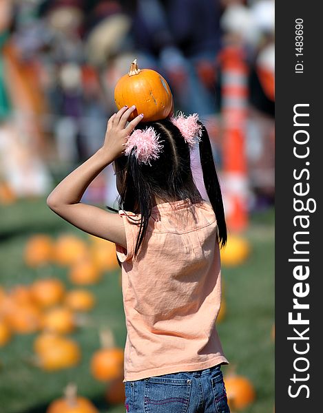 A little holding a small pumpkin on her head.  picture showing her back. A little holding a small pumpkin on her head.  picture showing her back.