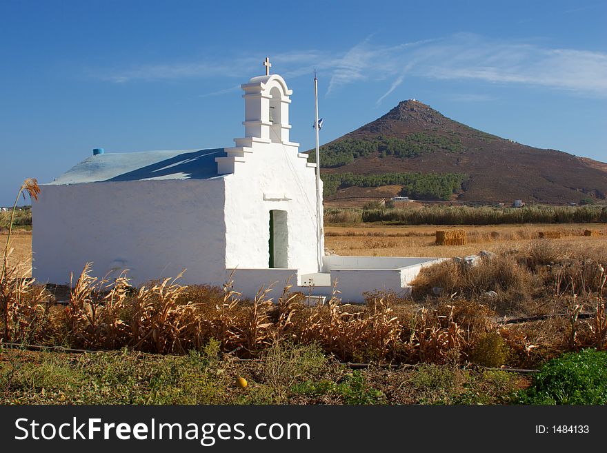 Greek Chapel in a filed with a hill behind