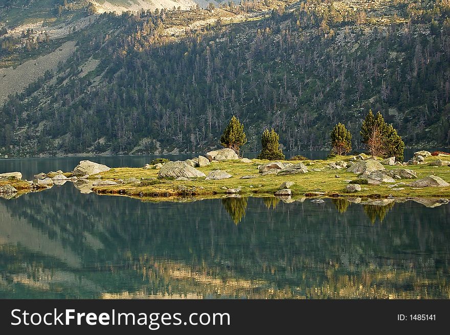 Small island and trees reflects in calm lake water (Pyrenees mountains). Small island and trees reflects in calm lake water (Pyrenees mountains)