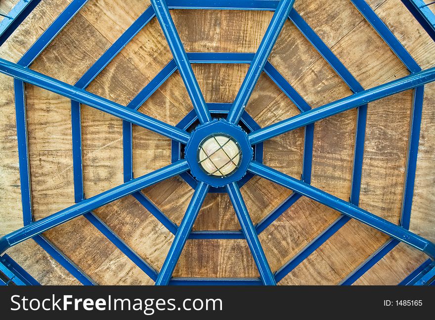 Architectural abstract-blue metal and wooden gazebo roof showing symmetry and resembling spider-web. Architectural abstract-blue metal and wooden gazebo roof showing symmetry and resembling spider-web