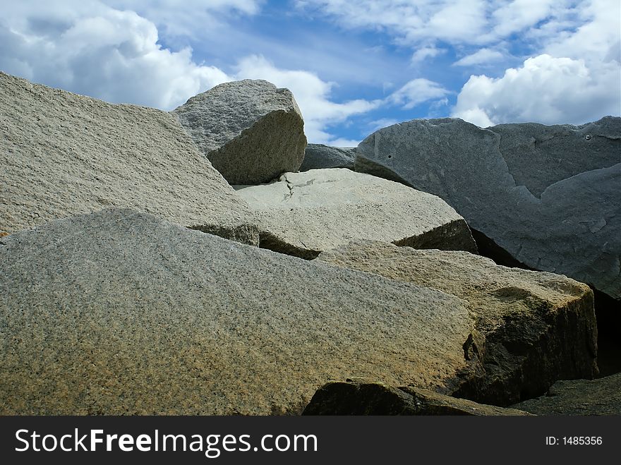 Large boulder rocks piled against a blue sky with clouds. Large boulder rocks piled against a blue sky with clouds