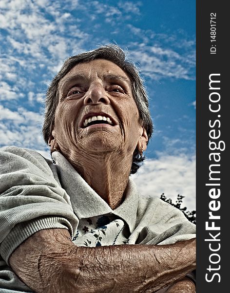 A closeup perspective portrait shot of a happy, elderly senior woman against a cloudy blue sky. A closeup perspective portrait shot of a happy, elderly senior woman against a cloudy blue sky.