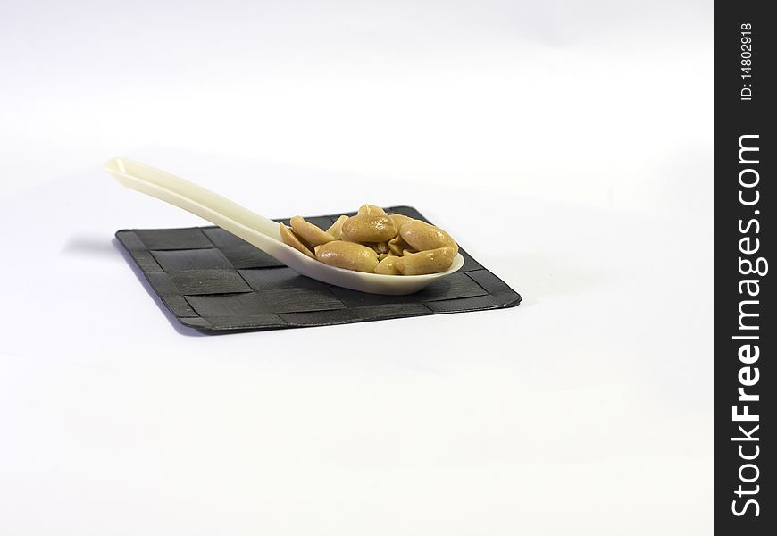 A spoonful of roasted, salted peanuts sitting in a spoon on a thatched mat. A spoonful of roasted, salted peanuts sitting in a spoon on a thatched mat.