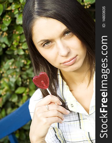 Young woman in an outdoors holding a lollipop in the shape of the heart. Sad. Young woman in an outdoors holding a lollipop in the shape of the heart. Sad