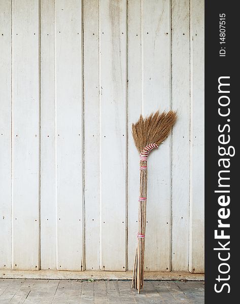 A broom leaning against wooden wall