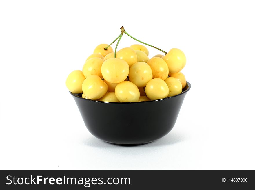 Yellow cherry in a black bowl isolated on white