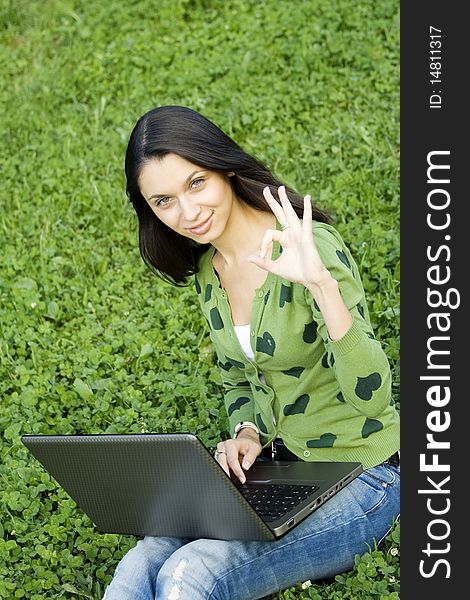 Young Caucasian woman with a laptop in the park on a green grass / meadow. Sign OK