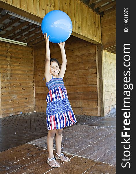 Little girl standing up, holding a big blue ball above her head, smiling. Little girl standing up, holding a big blue ball above her head, smiling