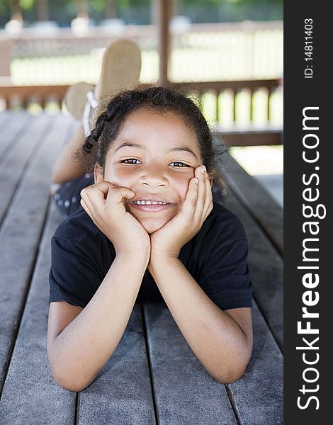 Little girl laying on a picnic table at the playground with her head cupped in her hands, smiling. Little girl laying on a picnic table at the playground with her head cupped in her hands, smiling