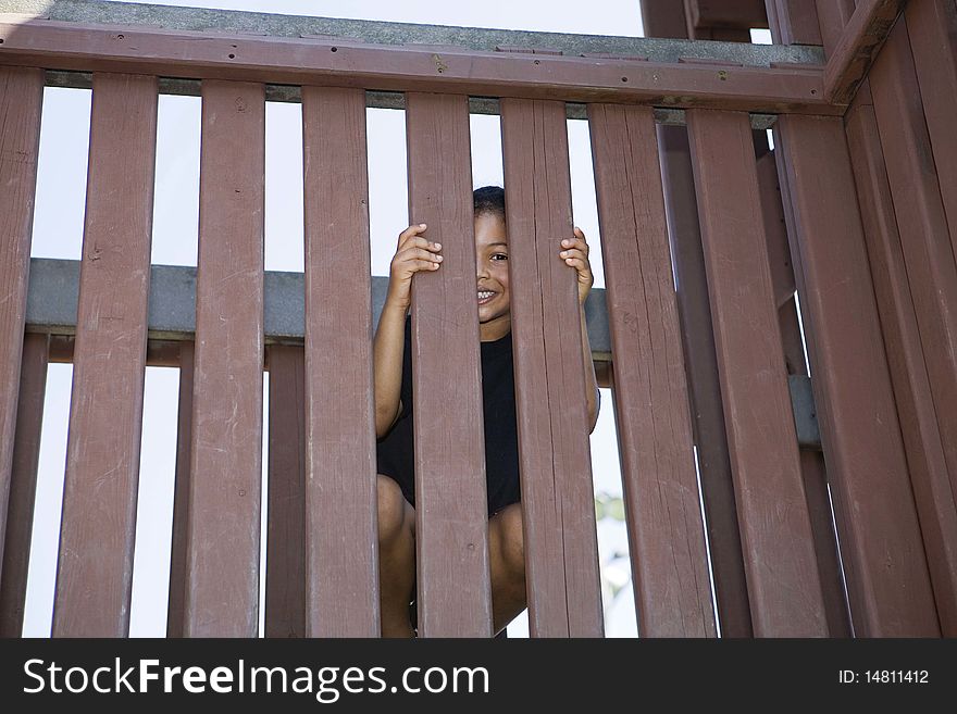 Little Girl Peeking Between Slats Of A Wooden Fenc