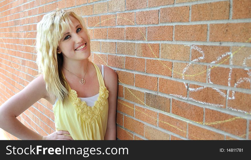 Happy young blond teenage girl standing in front of a brick wall smiling. Happy young blond teenage girl standing in front of a brick wall smiling.