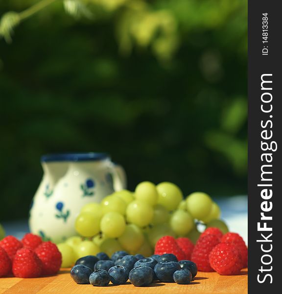 Fresh blueberries, raspberries and grapes on garden table. Focus on blueberies