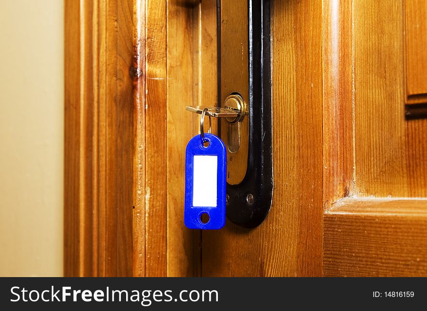 Key (with trinket for numbers) stick out in the lock of a wooden door (close up). Key (with trinket for numbers) stick out in the lock of a wooden door (close up)