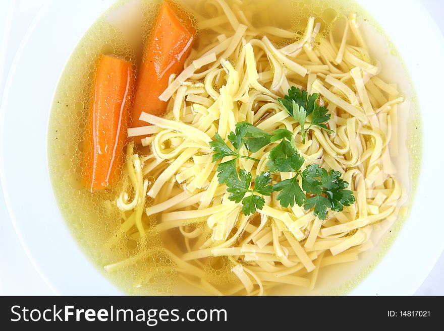 Chicken soup with macaroni and carrots decorated with parsley on a plate