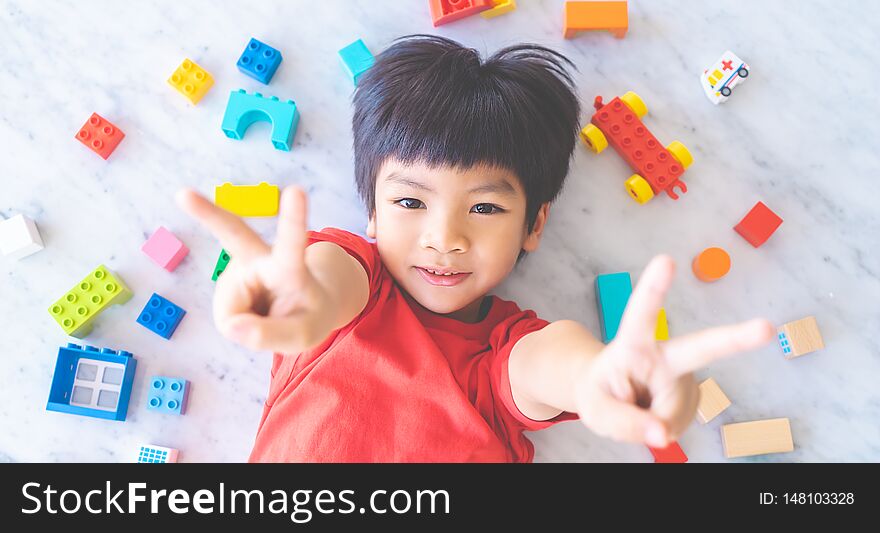 Boy surrounded by colorful toy blocks top view V shape hand for victory