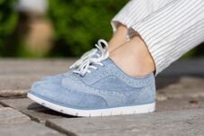 Girl Legs With Blue Sneakers On A Wooden Bench In The Park On A Spring Day Stock Photo