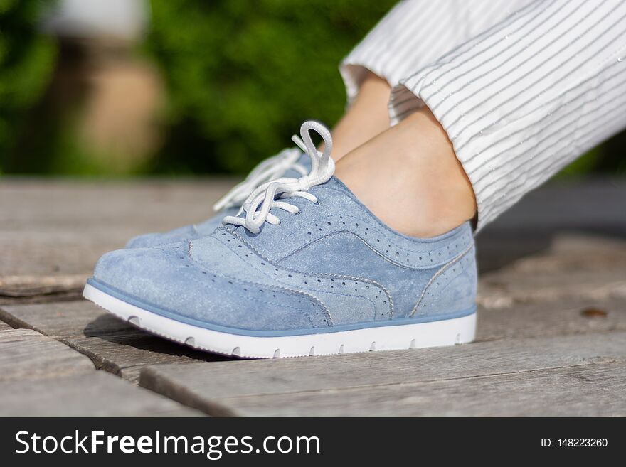 Girl legs with blue sneakers on a wooden bench in the park on a spring day