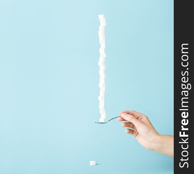 Female hand holding a spoon with column made of sugar cubes. Sweet life concept, minimal style. Sugar offering. Female hand holding a spoon with column made of sugar cubes. Sweet life concept, minimal style. Sugar offering