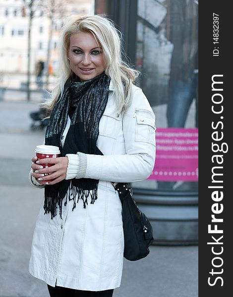 Young blond woman with drinking cup and a shoulder bag