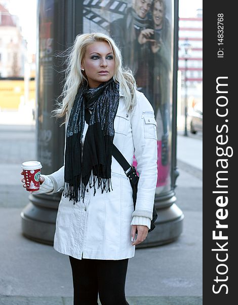 Young blond woman with drinking cup and a shoulder bag