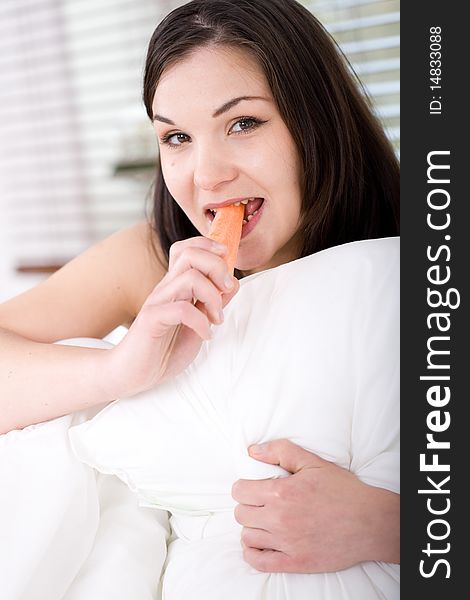 Young attractive brunette woman with carrot in bed. Young attractive brunette woman with carrot in bed