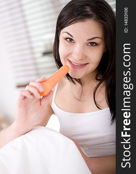 Young attractive brunette woman with carrot in bed. Young attractive brunette woman with carrot in bed