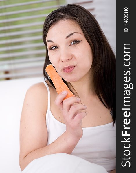 Young attractive brunette woman with carrot in bed. Young attractive brunette woman with carrot in bed