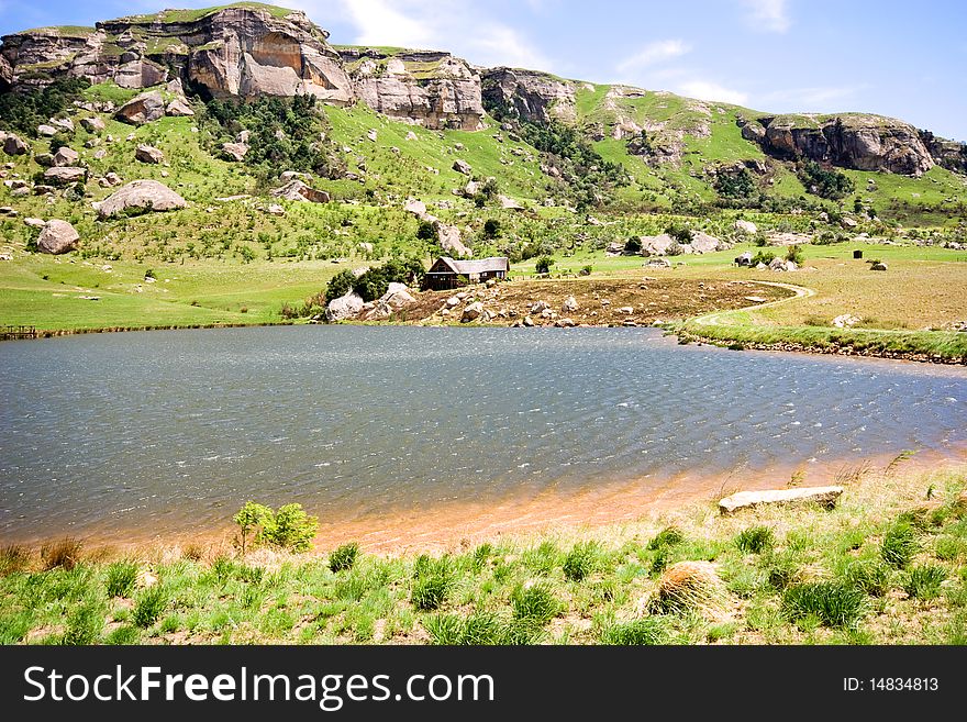 Mountain cottage in green grass at edge of dam