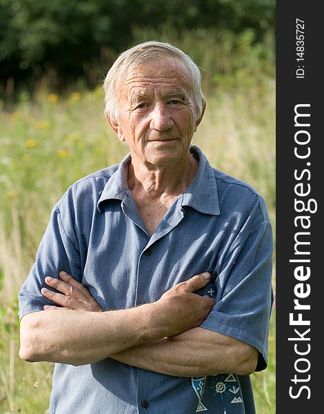 Portrait of the grey-haired elderly man in a blue shirt in the summer in village on the nature. Portrait of the grey-haired elderly man in a blue shirt in the summer in village on the nature
