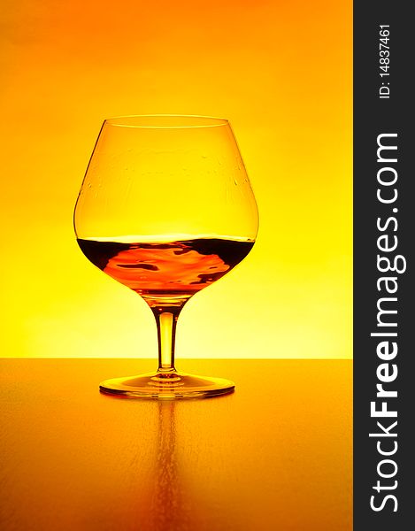 Glass of cognac on yellow background