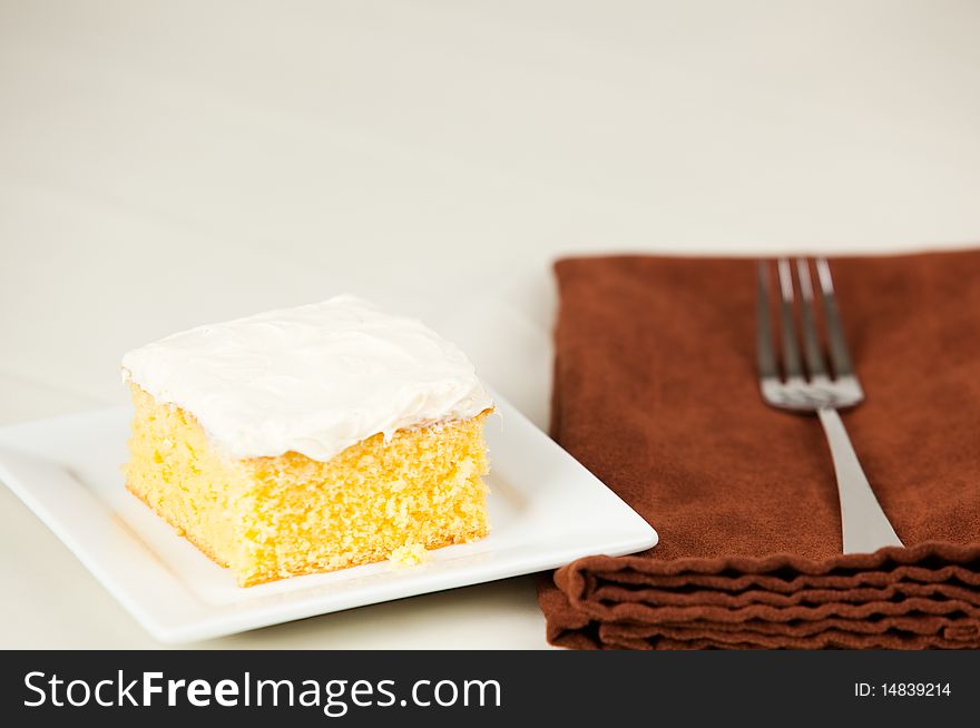 Piece of yellow cake on small white plate with napkin and fork. Piece of yellow cake on small white plate with napkin and fork