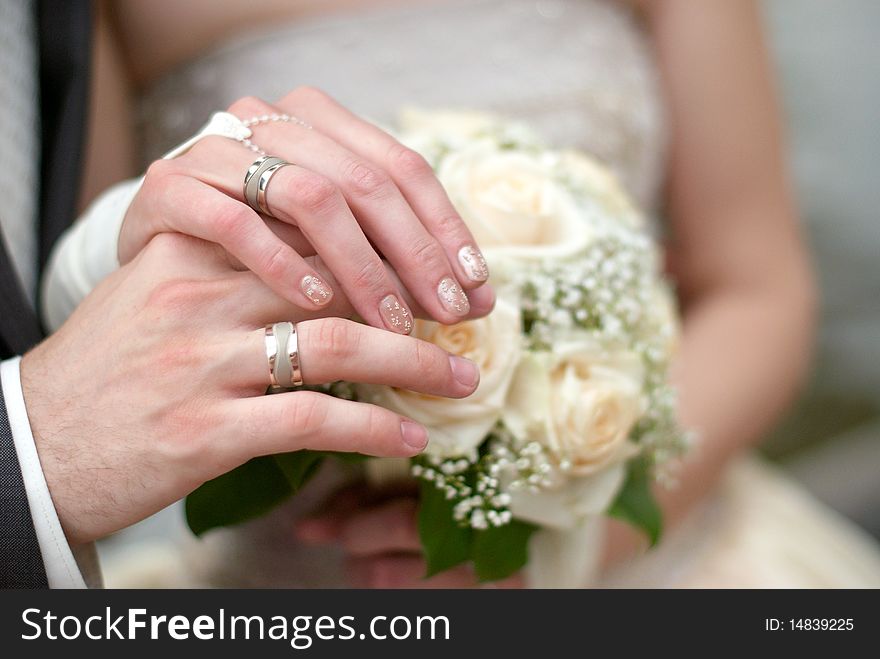 Bride and groom hands together on a roses bouquet. Bride and groom hands together on a roses bouquet