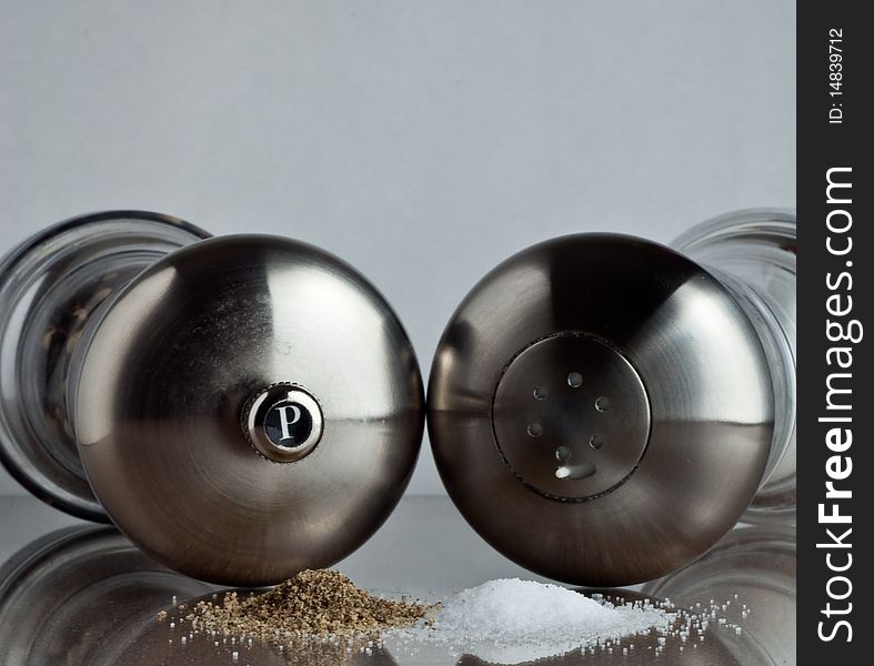 Salt and pepper shakers laying down behind a stack of their respective spices.