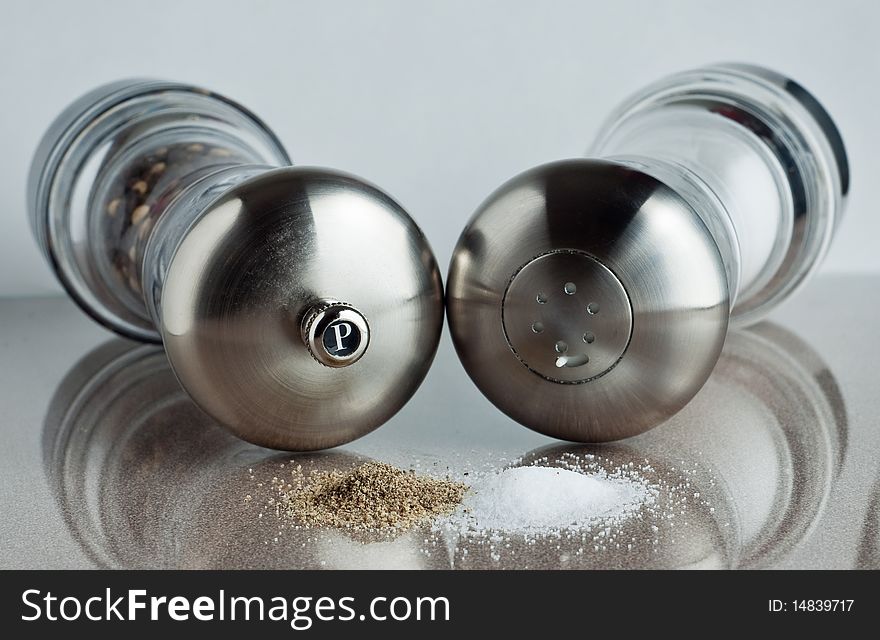 Salt and pepper shakers laying down behind a stack of their respective spices.