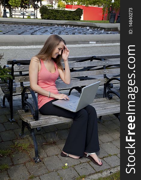 A student sitting on a park bench trying to think of what to do on her computer while she is relaxing at the park. A student sitting on a park bench trying to think of what to do on her computer while she is relaxing at the park.