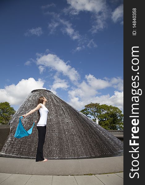 A woman holding her blue sarong while standing near a beautiful water fountain letting the breeze blow her sarong. A woman holding her blue sarong while standing near a beautiful water fountain letting the breeze blow her sarong.