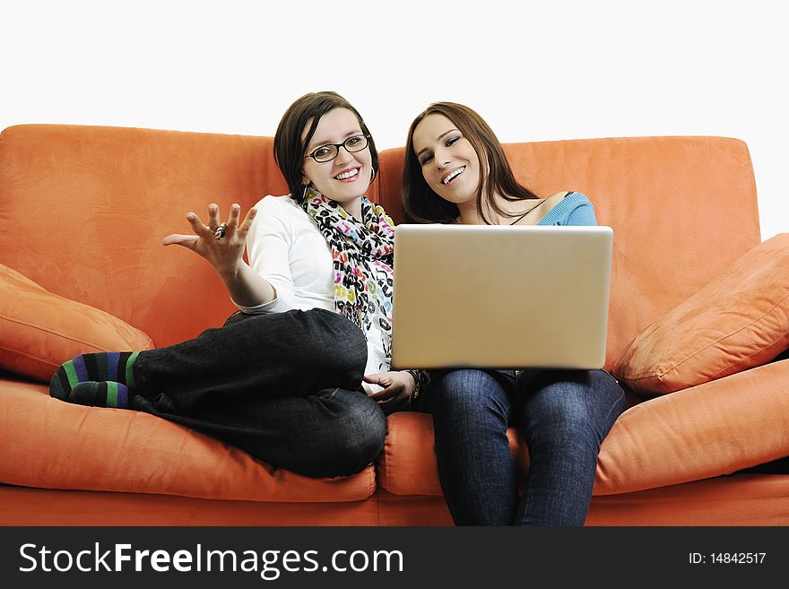 Two happy young woman working on laptop computer on red sofa isolated on white. Two happy young woman working on laptop computer on red sofa isolated on white