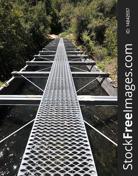 A walkway over a waterway made of metal and wood in the woods. A walkway over a waterway made of metal and wood in the woods