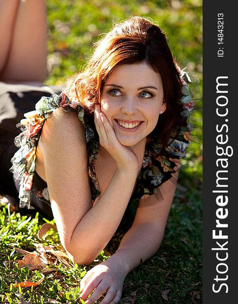 Beautiful young woman is lying on the grass and smiling to the side. Vertical shot. Beautiful young woman is lying on the grass and smiling to the side. Vertical shot.