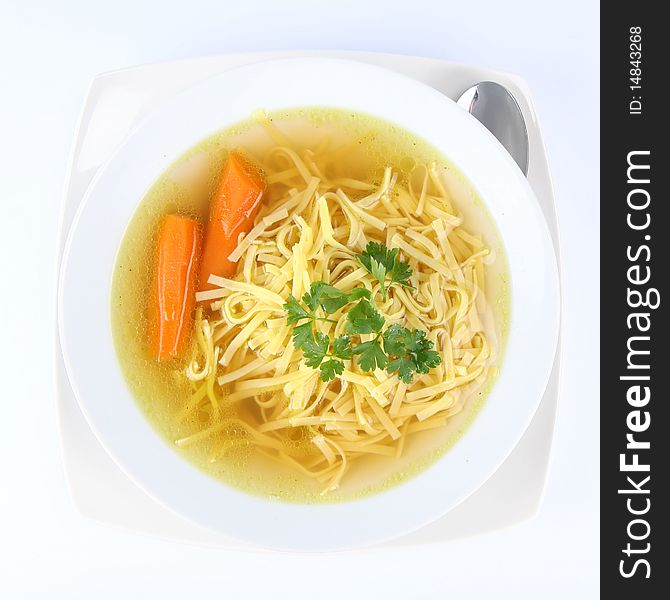 Chicken soup with macaroni and carrots decorated with parsley on a plate with a spoon