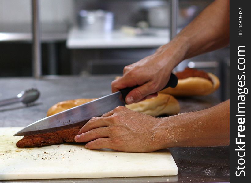 A man cutting breaded chicken up for a chicken parmesan sandwich.